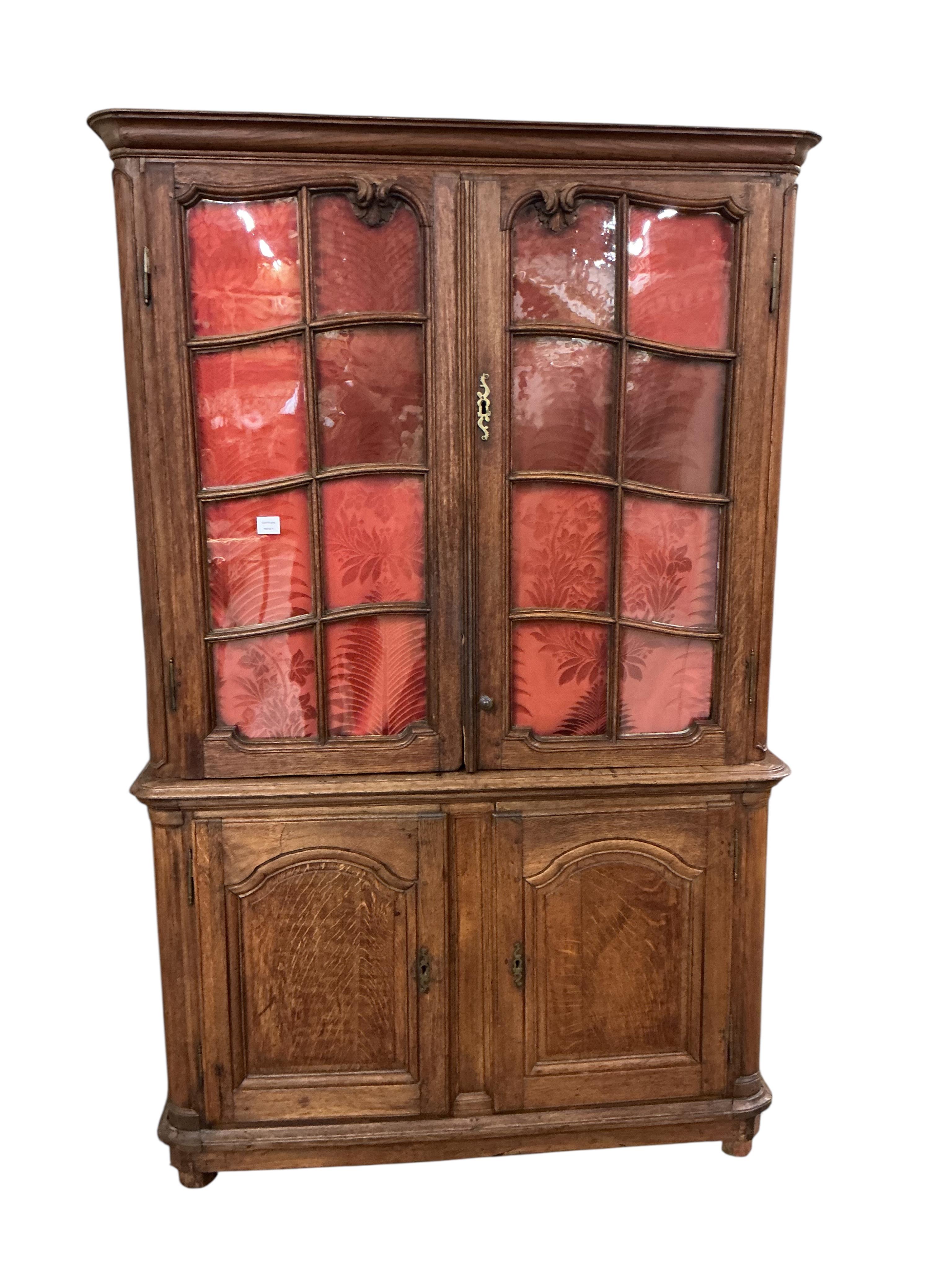 An early 19th century French Burgundian oak cabinet with two glazed doors over two arched panelled door, width 130cm, depth 49cm, height 206cm